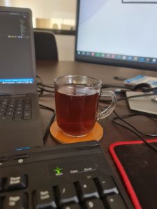 Black tea is in between the laptop, the external keyboard, and the monitor. 