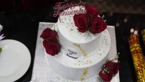 An anniversary cake in white adorned with red roses.